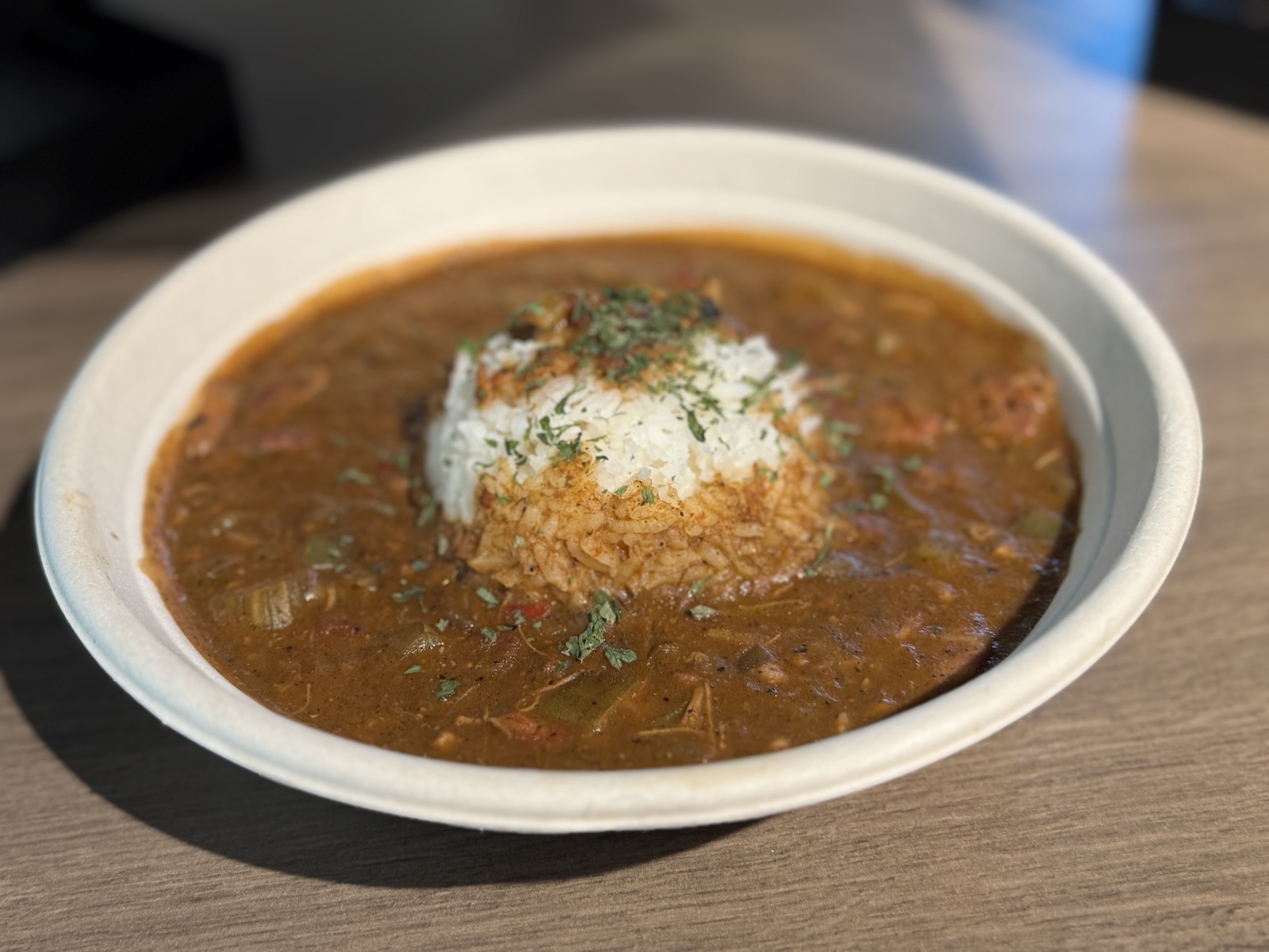 A disposable bowl filled with gumbo and a scoop of rice