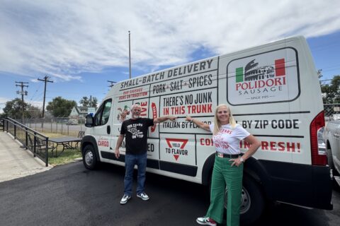 A man in a black T-shirt and a woman in a white T-Shirt and green pants stand in front of a Polidori Sausage van.