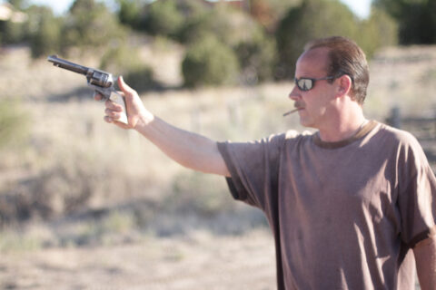 A man with a cigarette shoots a handgun
