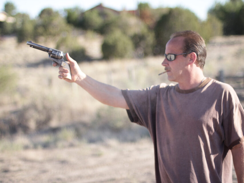 A man with a cigarette shoots a handgun