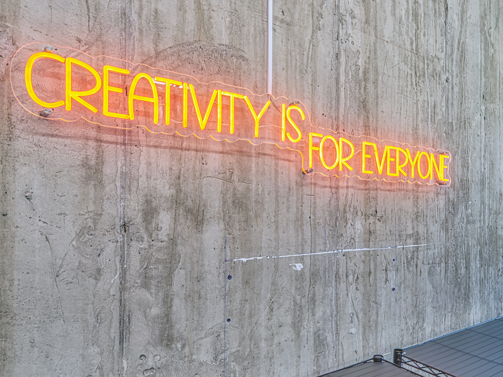 A sign that says Creativity Is For Everyone in orange neon
