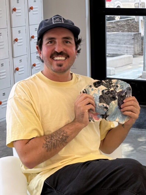 Aaron Cummins in a yellow shirt, holding a pottery self-portrait