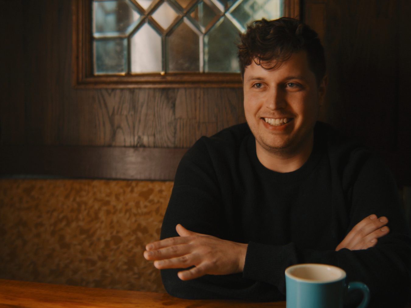A man smiles with a cup of coffee in a booth