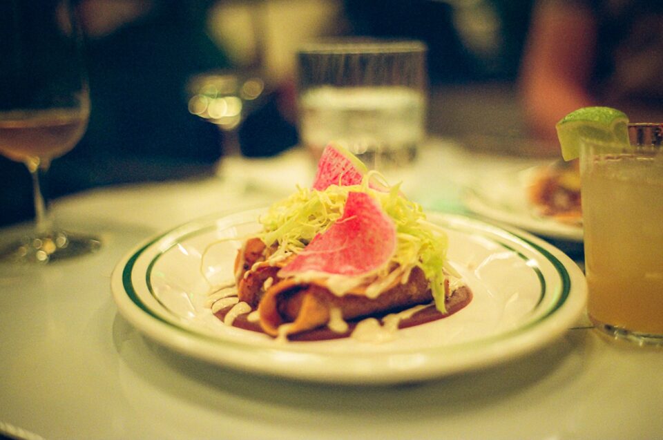 Two flautas on an oval plate topped with shredded cabbage and watermelon radish slices