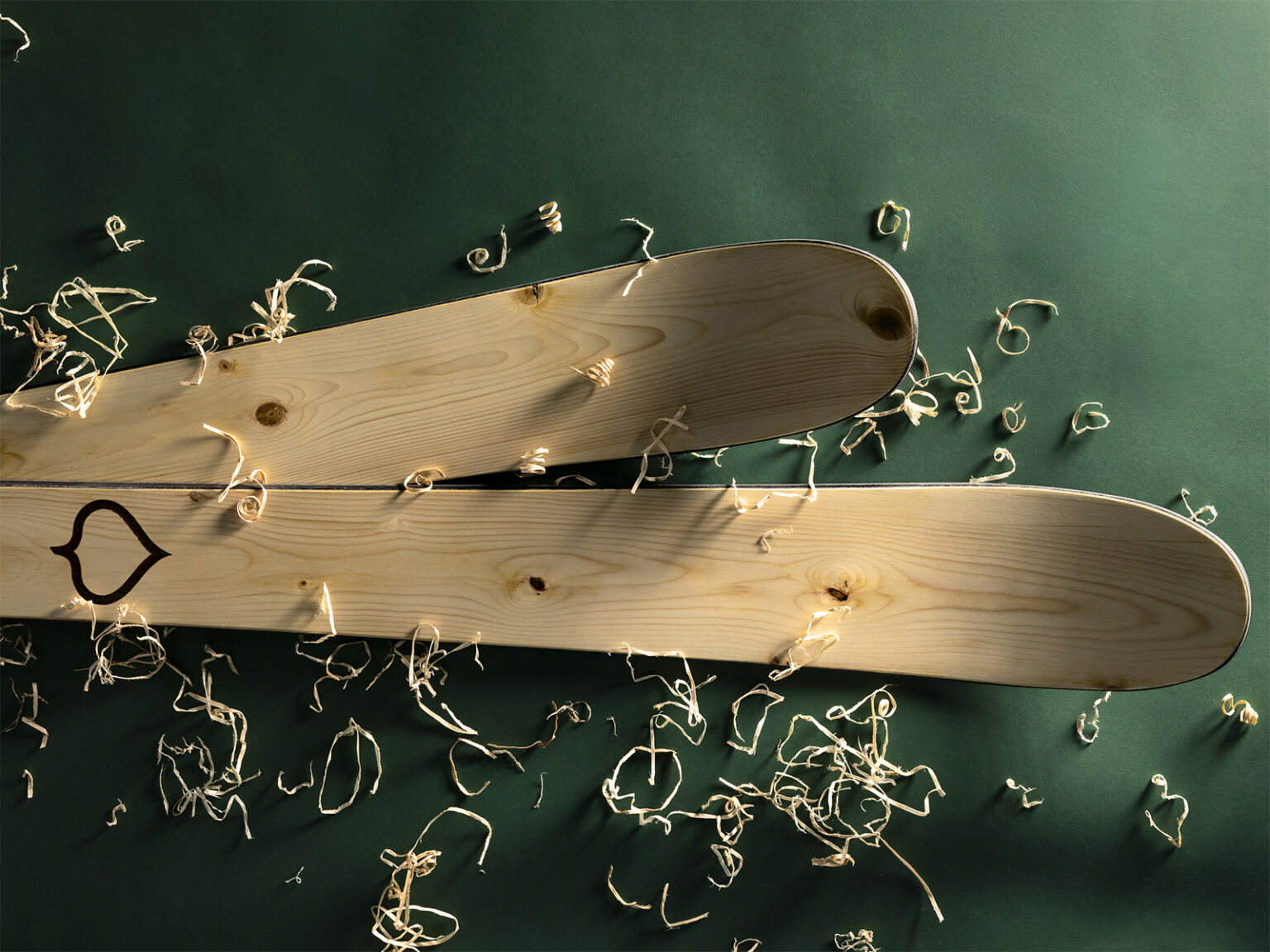 A pair of Wagner Custom Skis Hero’s Spruce Skis on a green background with wood shavings