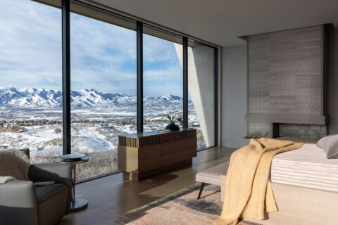 A modern bedroom with large windows facing snowy mountains