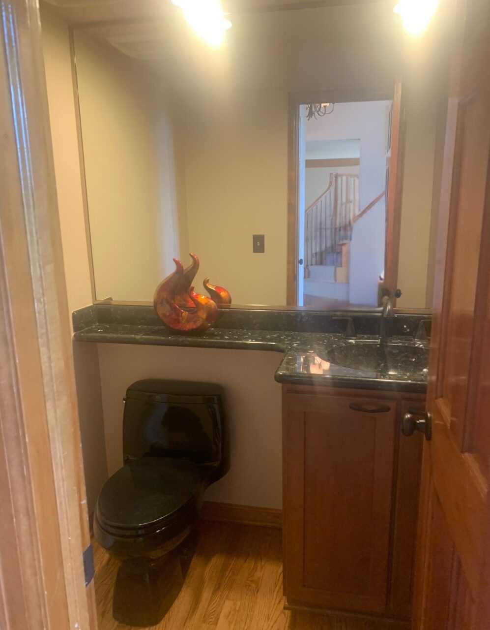 Dated bathroom with a black toilet and oversize mirror