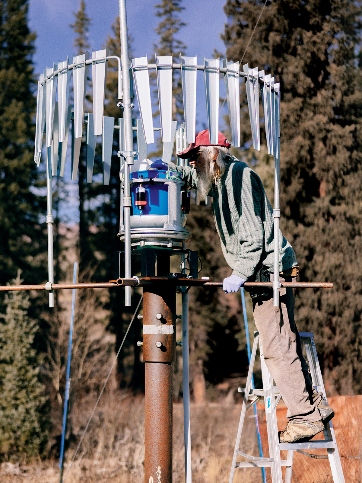 A man on a ladder in the woods measuring climate data
