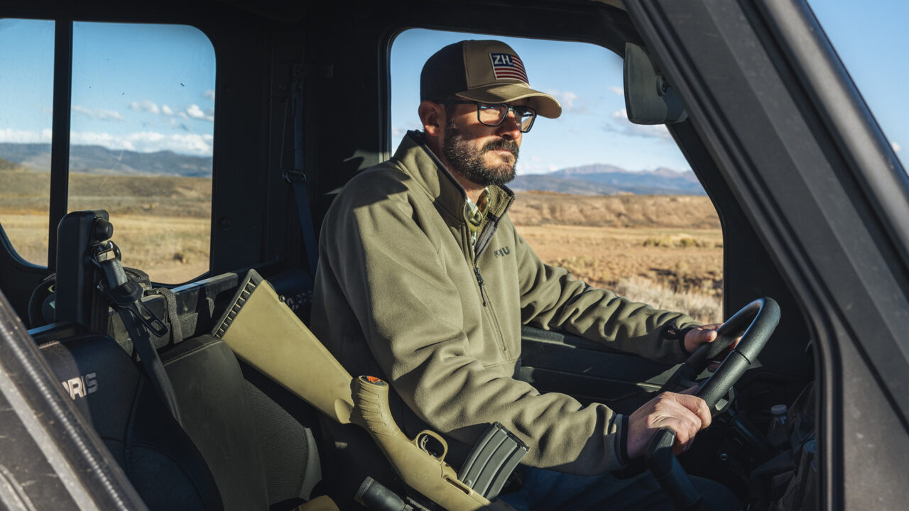 A man with a rifle drives a truck on a ranch