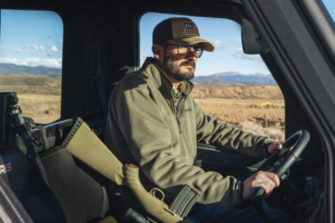 A man with a rifle drives a truck on a ranch