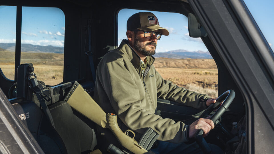 A man with a rifle drives a truck on a ranch