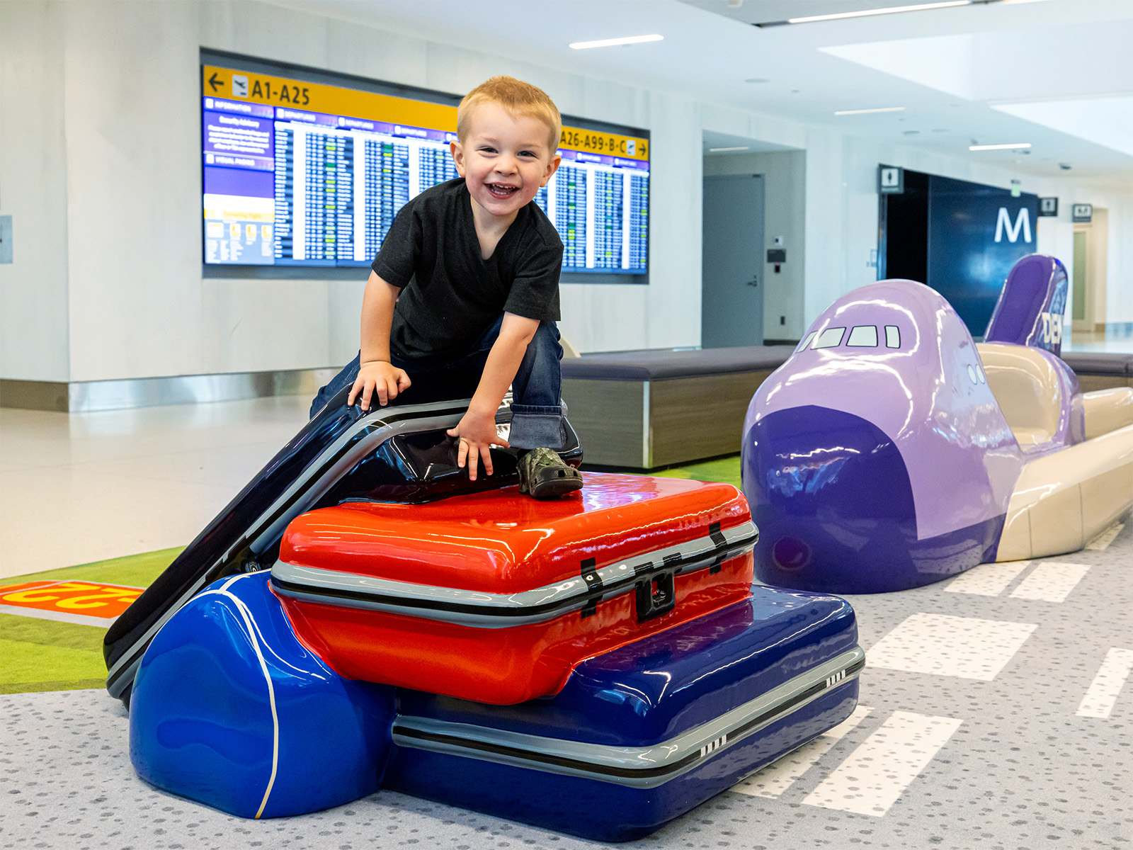 A kid on a sculpture of luggage by Soft Play at Denver International Airport