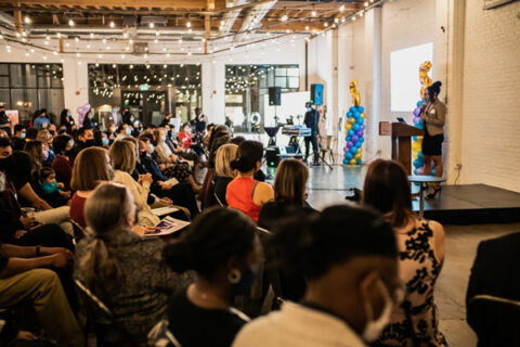 A room full of people sitting down and listening to a speaker on stage.