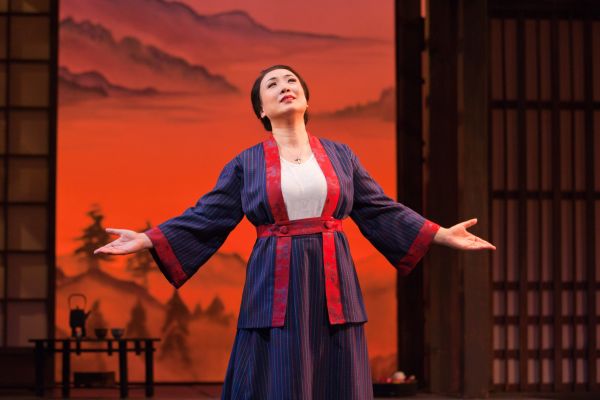 An Asian woman standing on a stage singing opera.