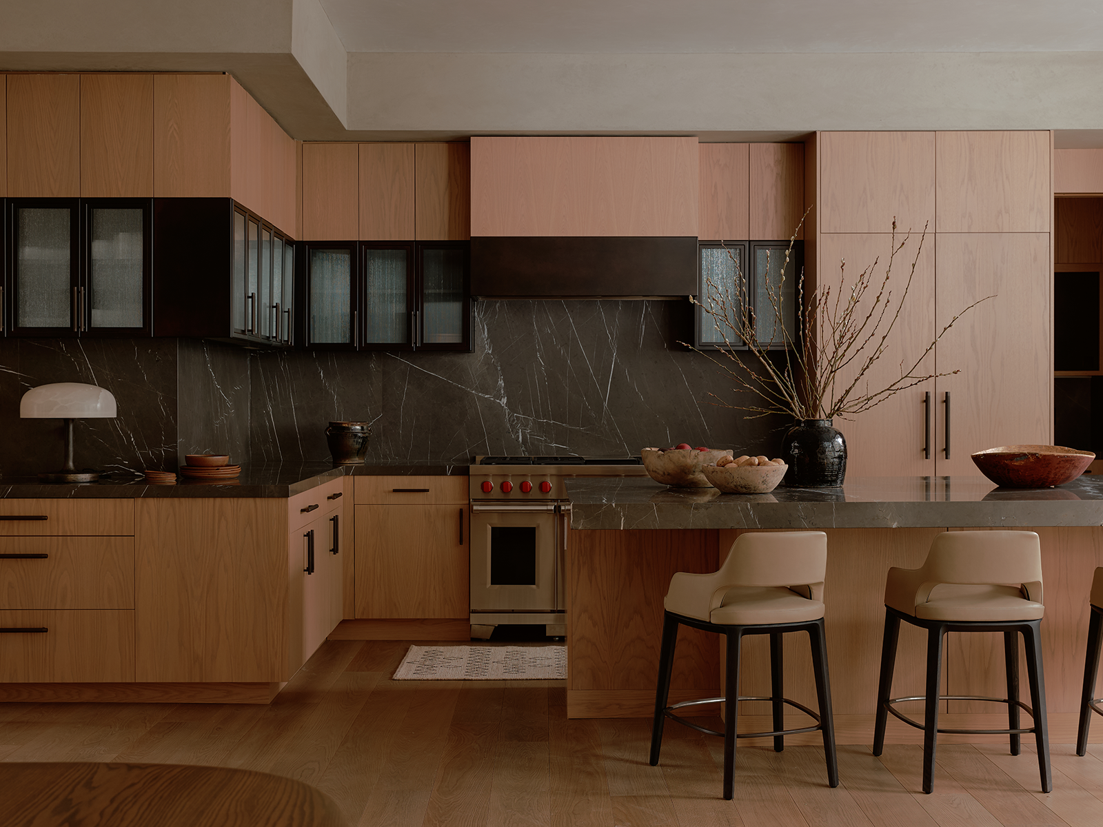 Kitchen with brown cabinetry, cream-hued leather stools, and black marble countertops