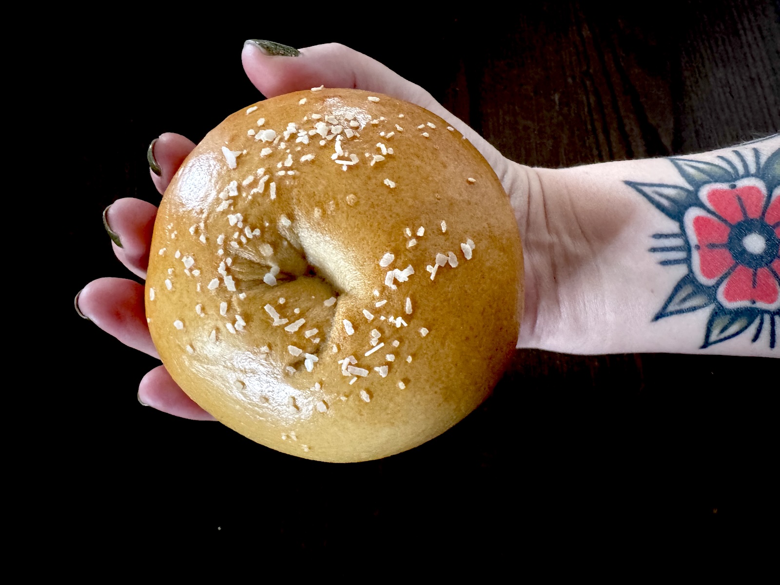 A hand holding an unsliced salt-crusted bagel