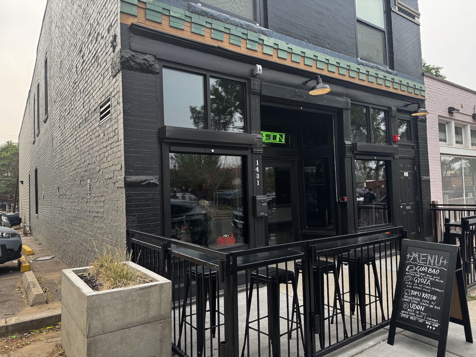 An old two-story building with new black paint and a green neon sign with part of the word pigeon visible.
