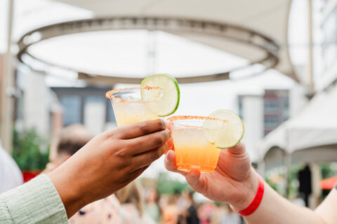 Two cocktails being held outside at a foodie event.