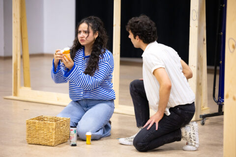 A young woman and man sitting on the floor in front of a basket with medication bottles.
