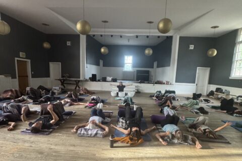 A room of people laying down on yoga mats listening to sound bowls.