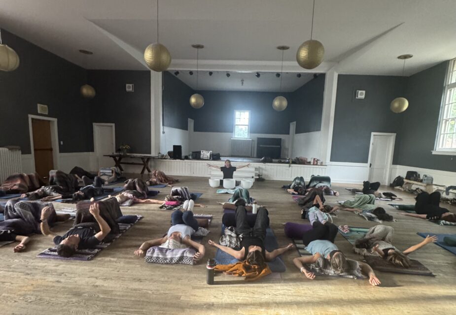 A room of people laying down on yoga mats listening to sound bowls.