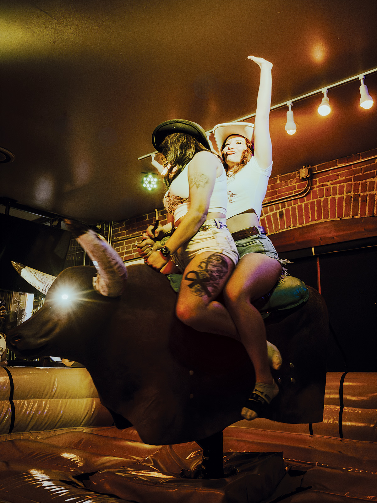 Two gals riding a mechanical bull at Belles & Boots