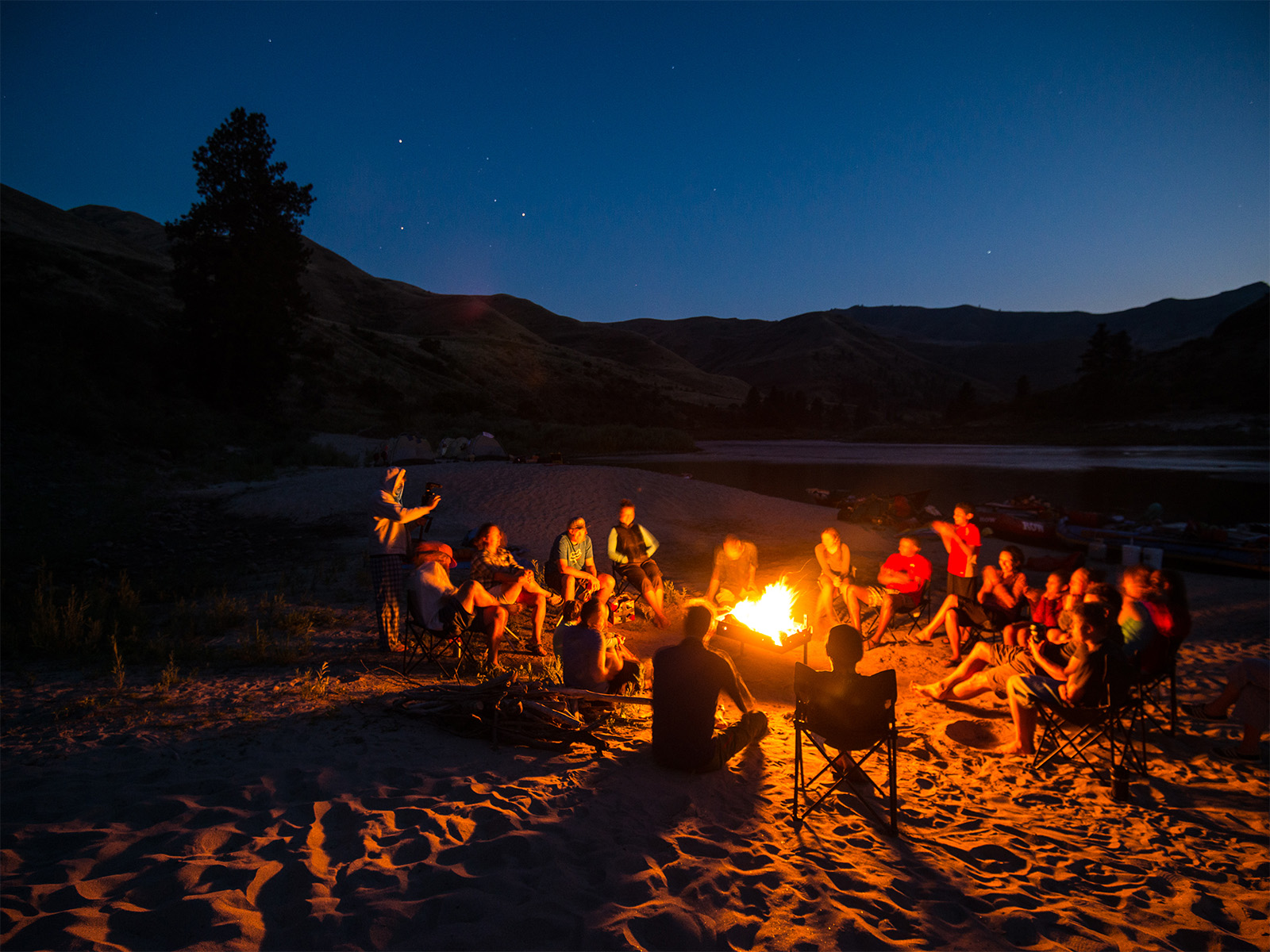 People circled around a campfire on a sandy beach along Idaho’s Lower Salmon River