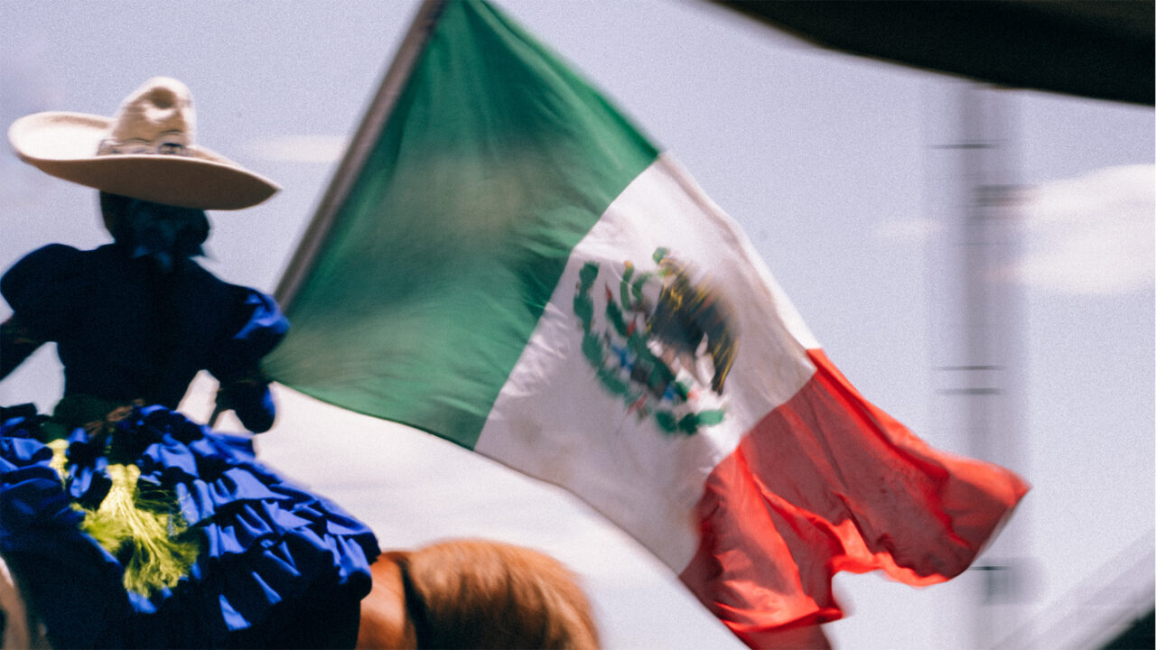 A charro handling a Mexican flag on horseback