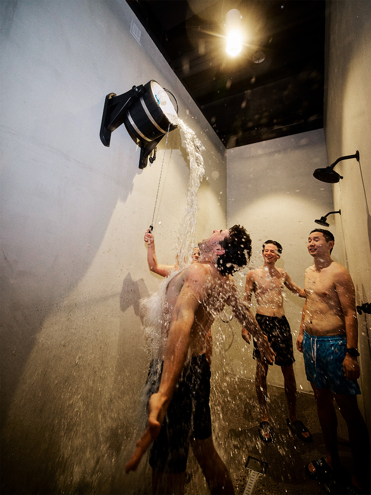 A topless man dumps cold water on himself while his topless buddies look on