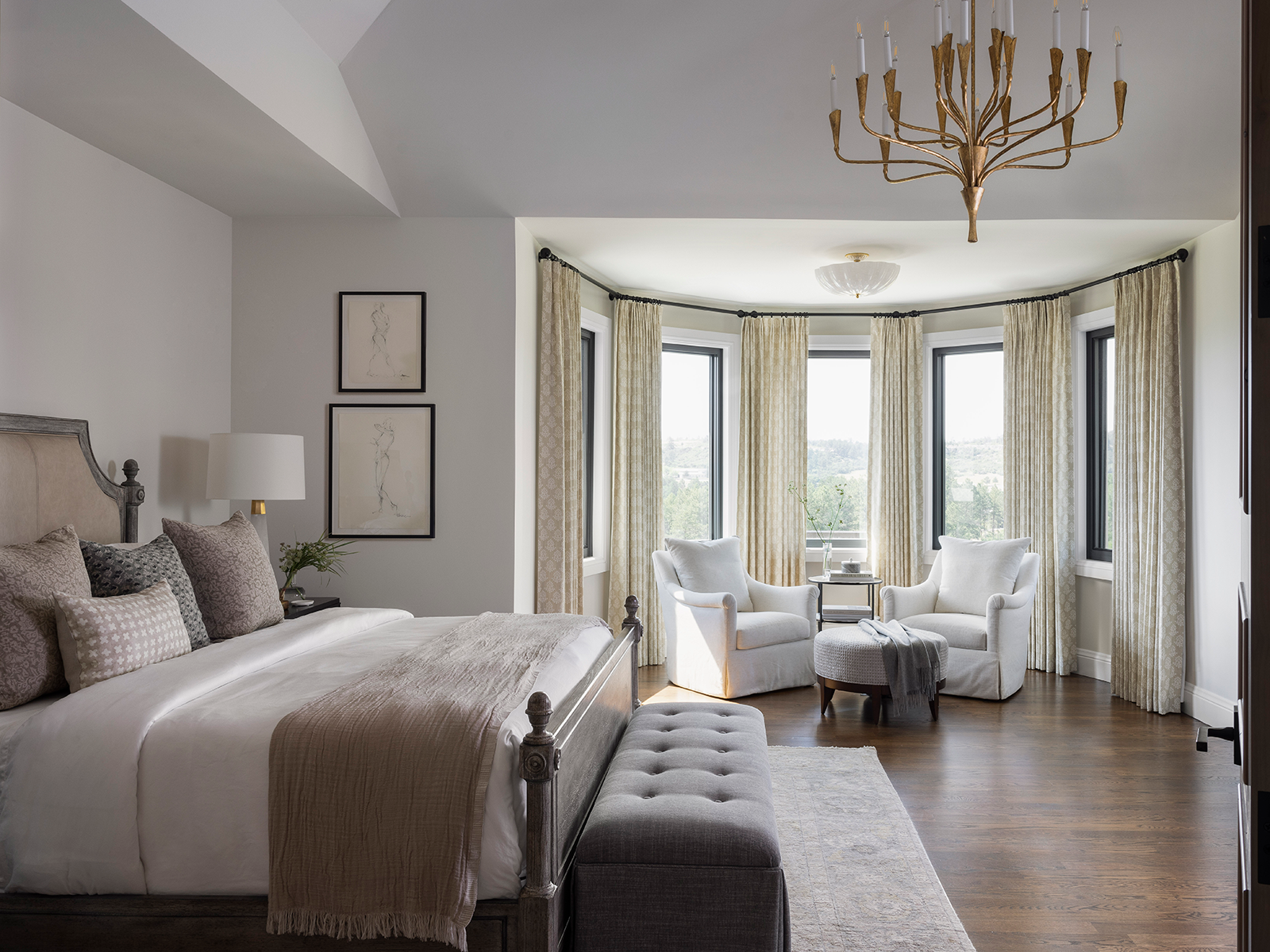 Primary bedroom with cream furniture and a sitting area by bay windows