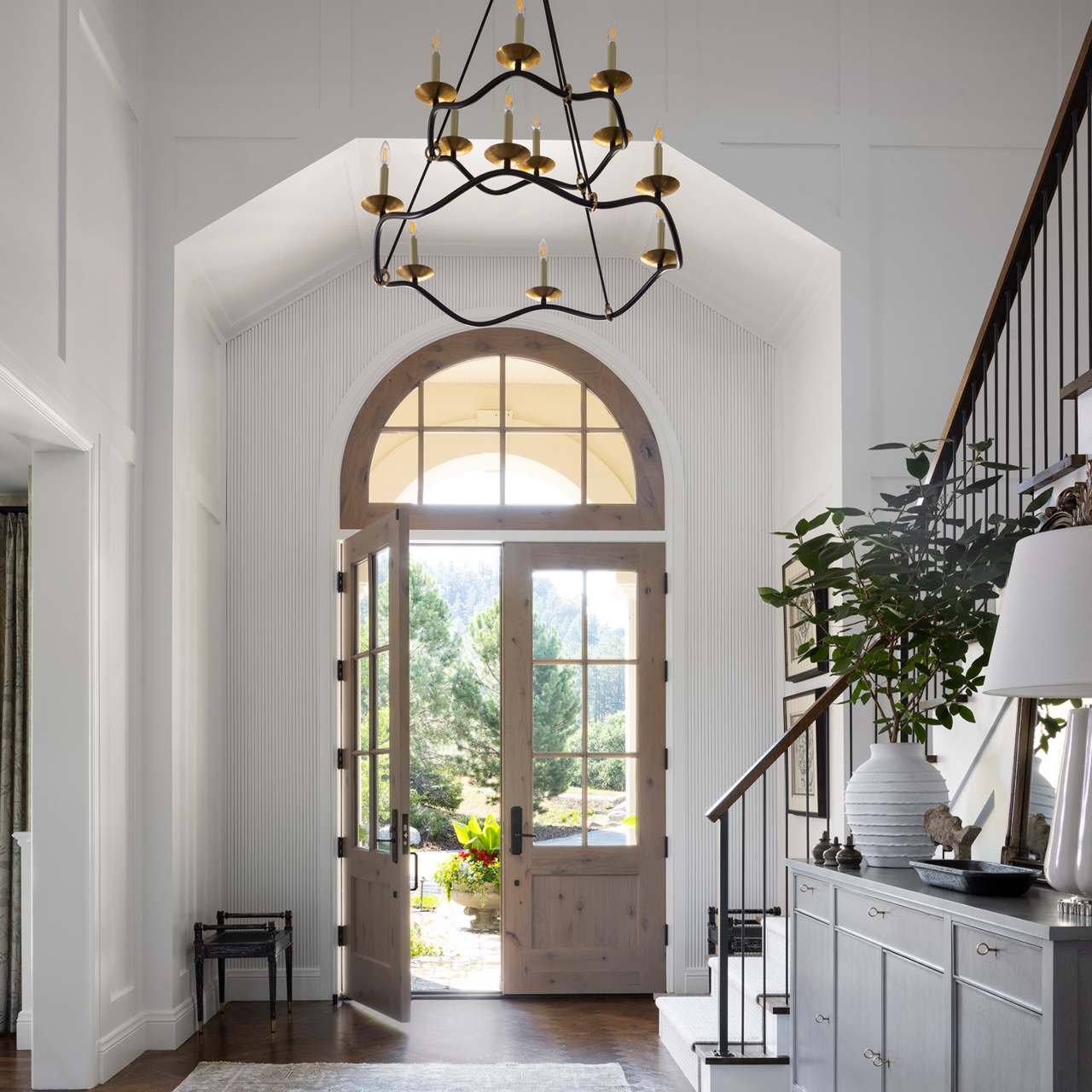White entryway with two wood doors and a larger tiered hanging chandelier