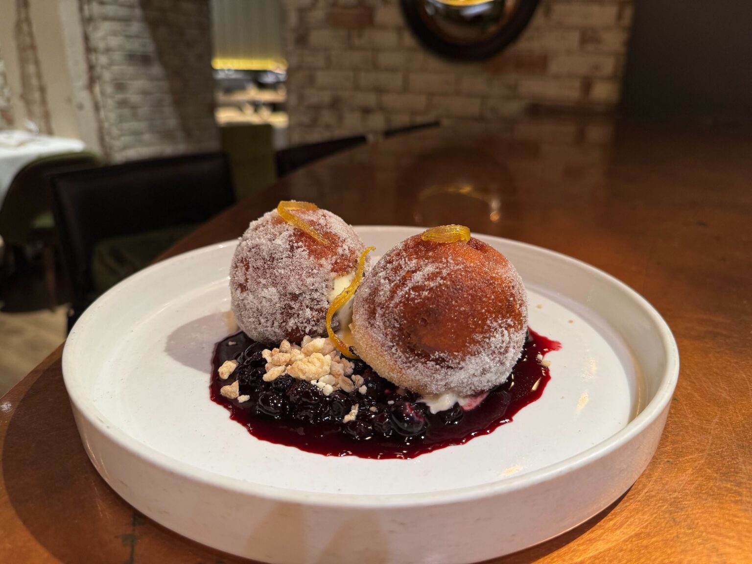Two large doughnut holes with sugar on top and blueberry sauce on a white plate