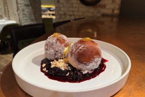 Two large doughnut holes with sugar on top and blueberry sauce on a white plate