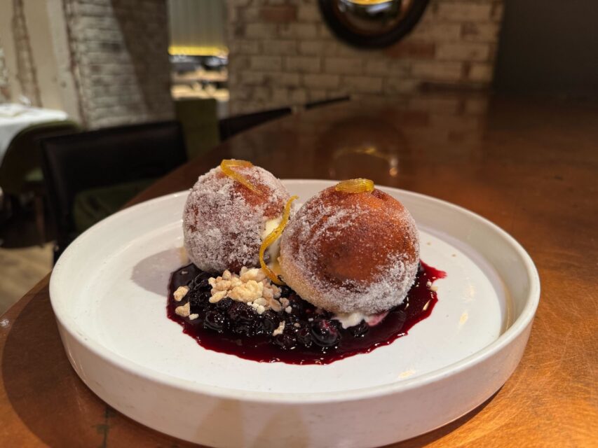 Two large doughnut holes with sugar on top and blueberry sauce on a white plate