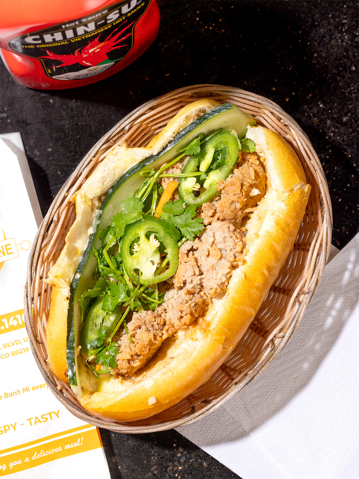 A banh mi loaded with jalapeños in a basket
