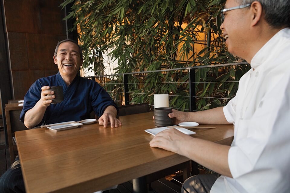 Two Japanese chefs sharing drinks at a restaurant table