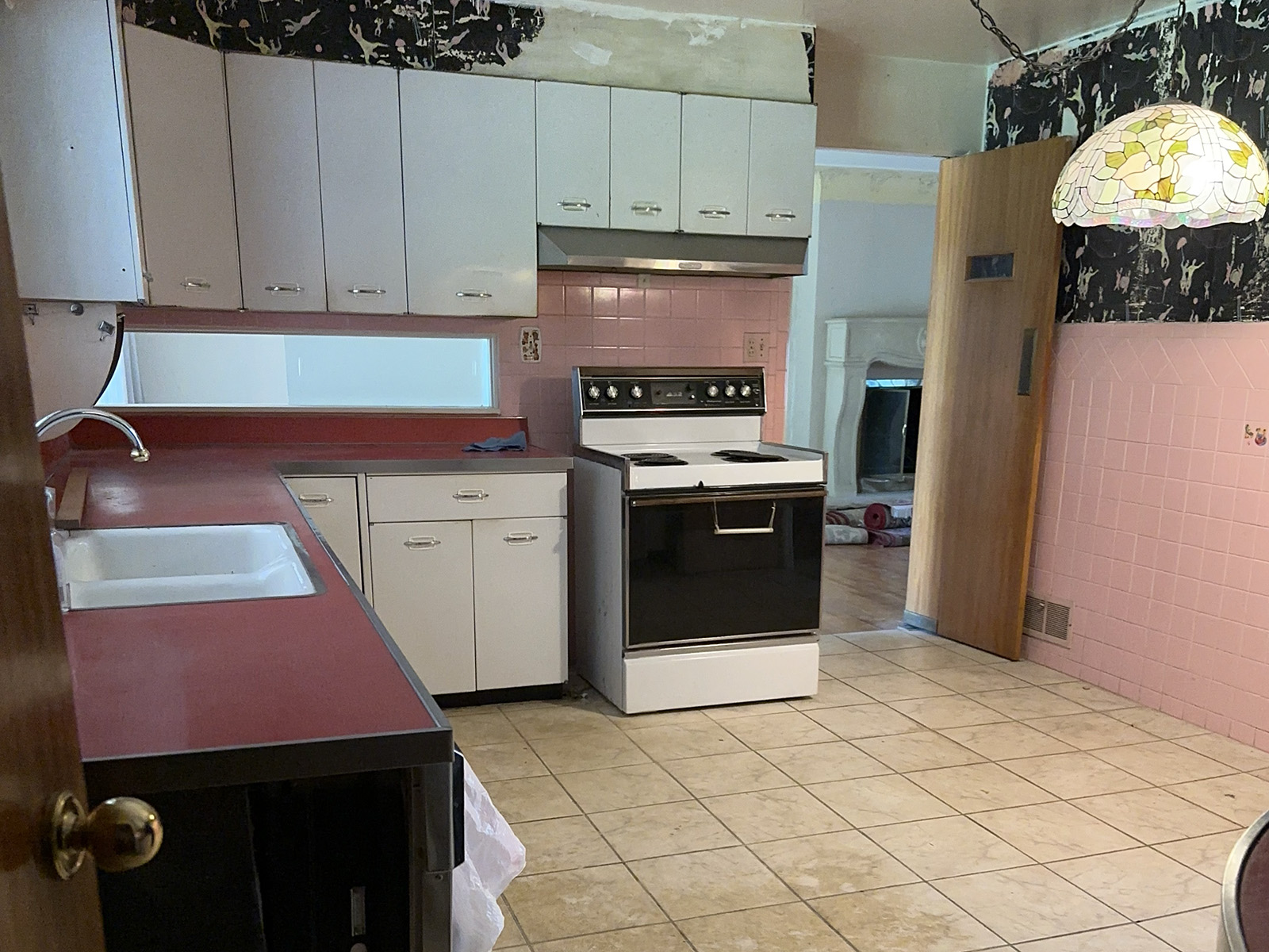Old kitchen with pink walls, white cabinets, and red countertops