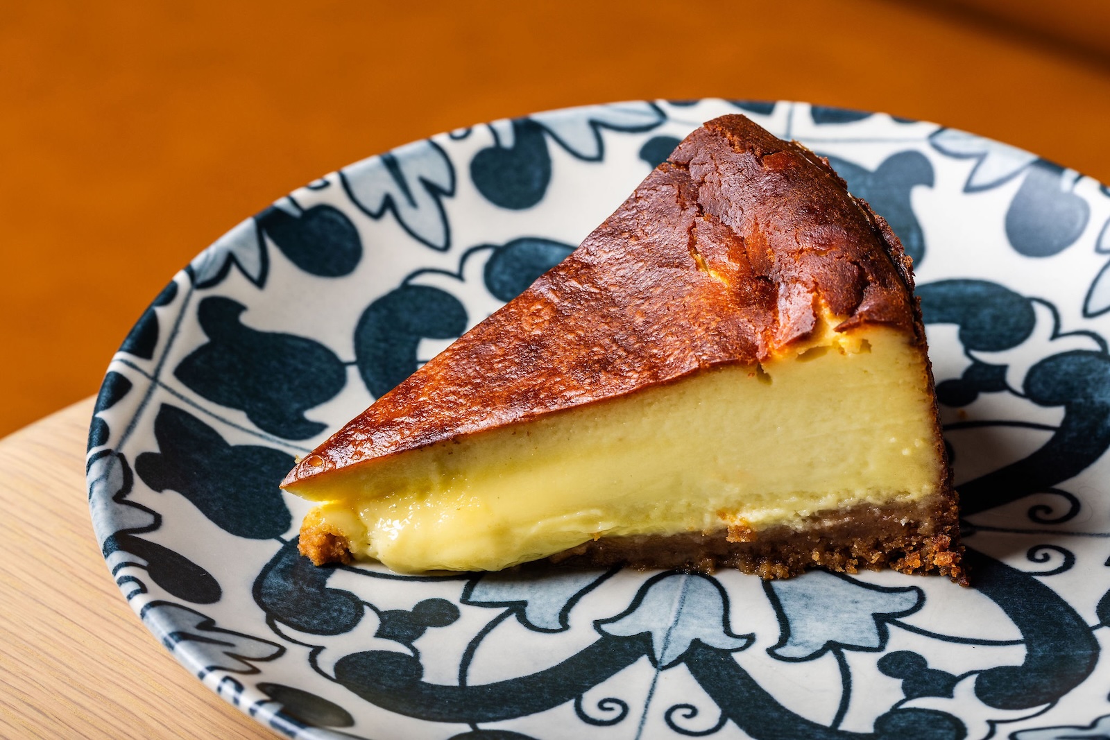 A slice of basque cheesecake with a dark top crust on a blue and white plate