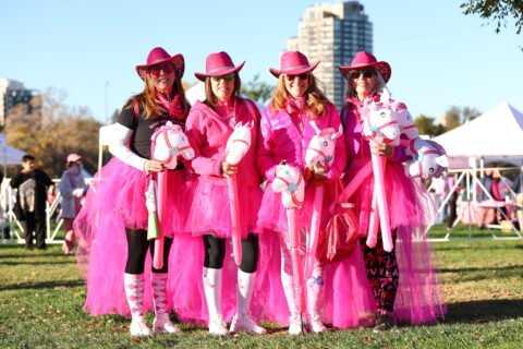 Four women dressed in pink wearing pink cowboy hats posing together outside.