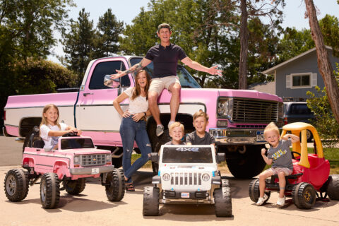 Taylor Calmus (aka Dude Dad) with his wife and four children in front of a pink truck (real) and three children’s vehicles