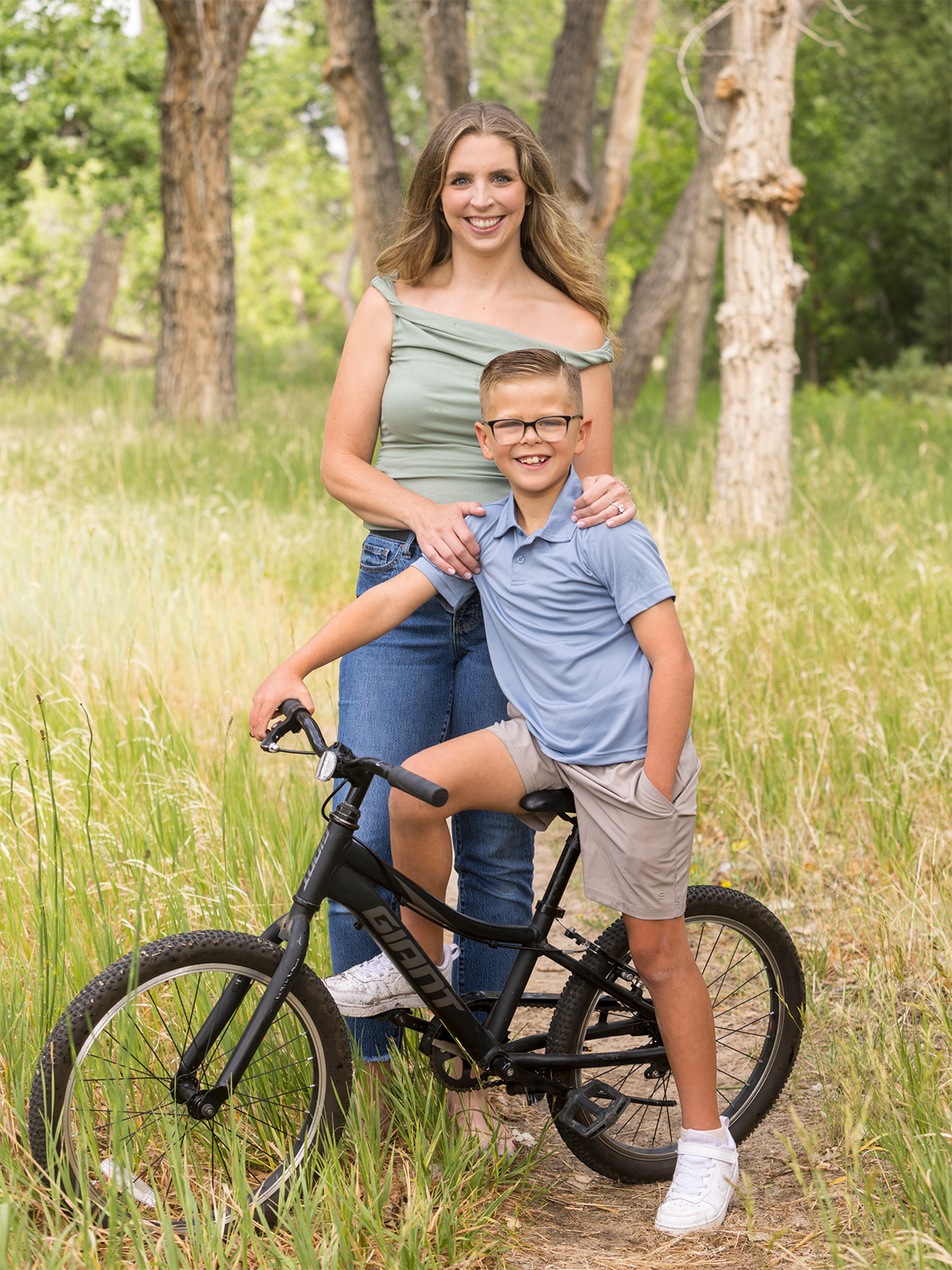 A woman standing with a young boy on a bicycle