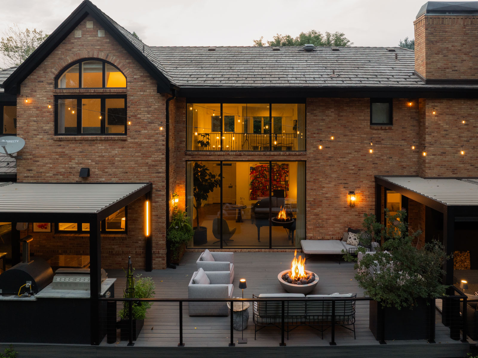 Back exterior of a two-story home with a large wall of windows and a deck with a fire pit