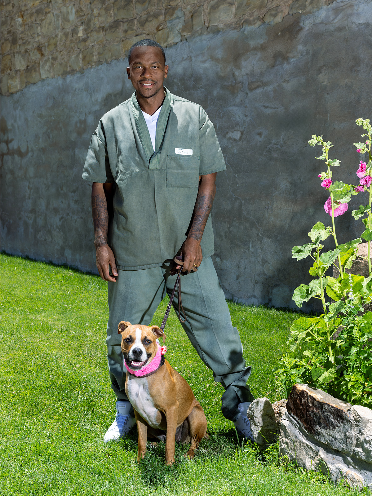 Robert Ray wears prison garb and holds the leash of a brown and white dog with a pink crocheted collar