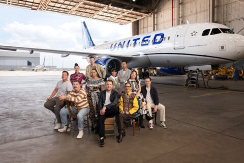 A group of chefs stand in front of a United Airlines plane in a hangar.