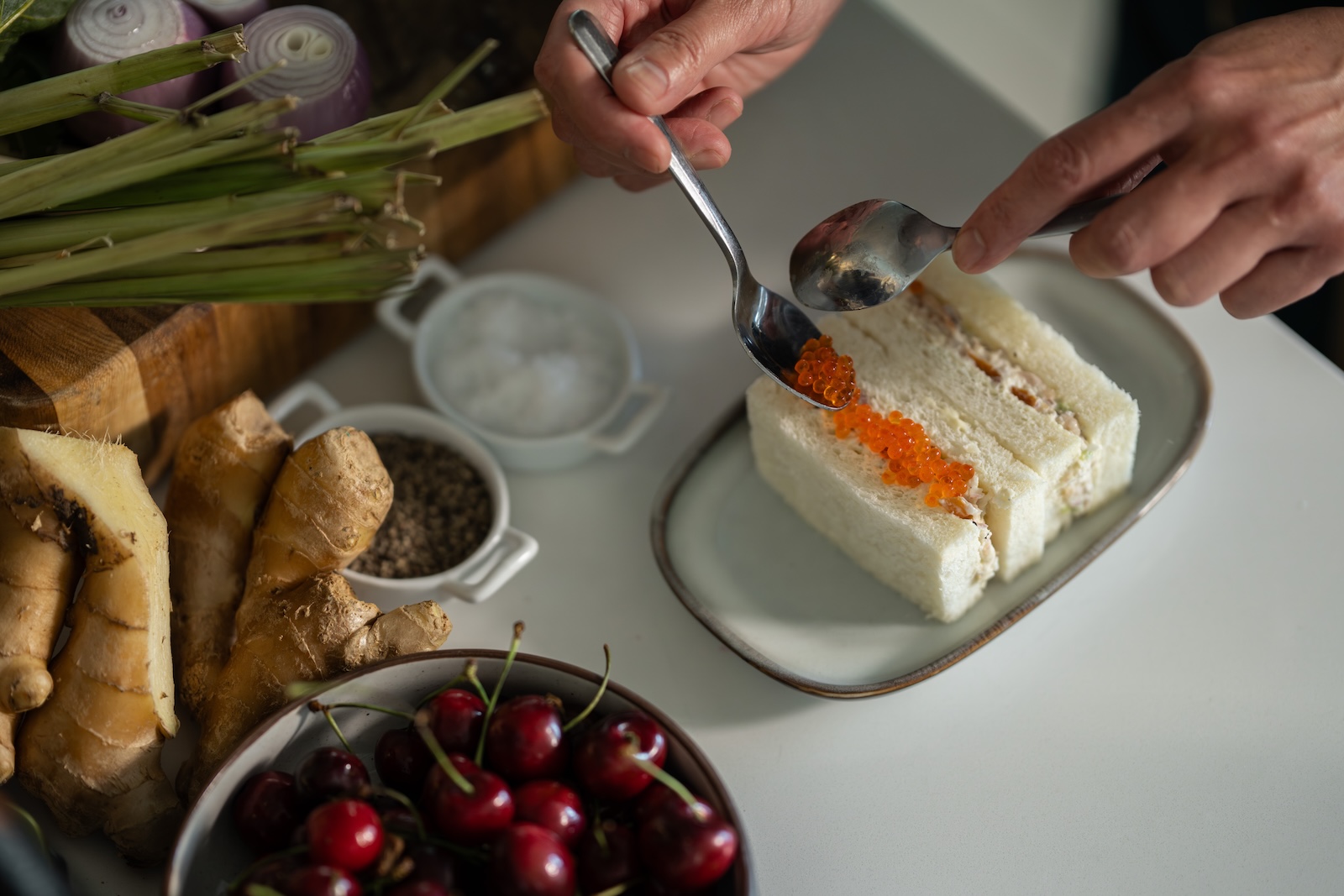 A Japanese-style white bread sandwich with a hand spooning organge trout roe onto it.