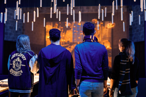 Four people stand in the Great Hall of Hogwarts