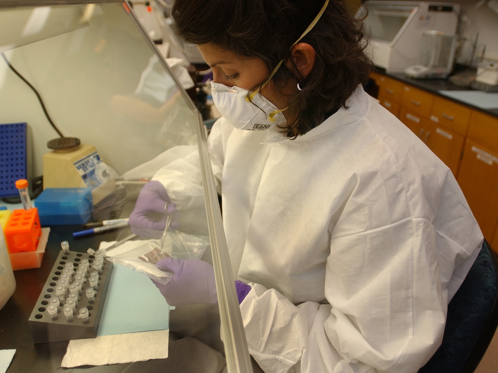Missy Woods, in a white mask and lab coat, cuts a plastic bag with scissors