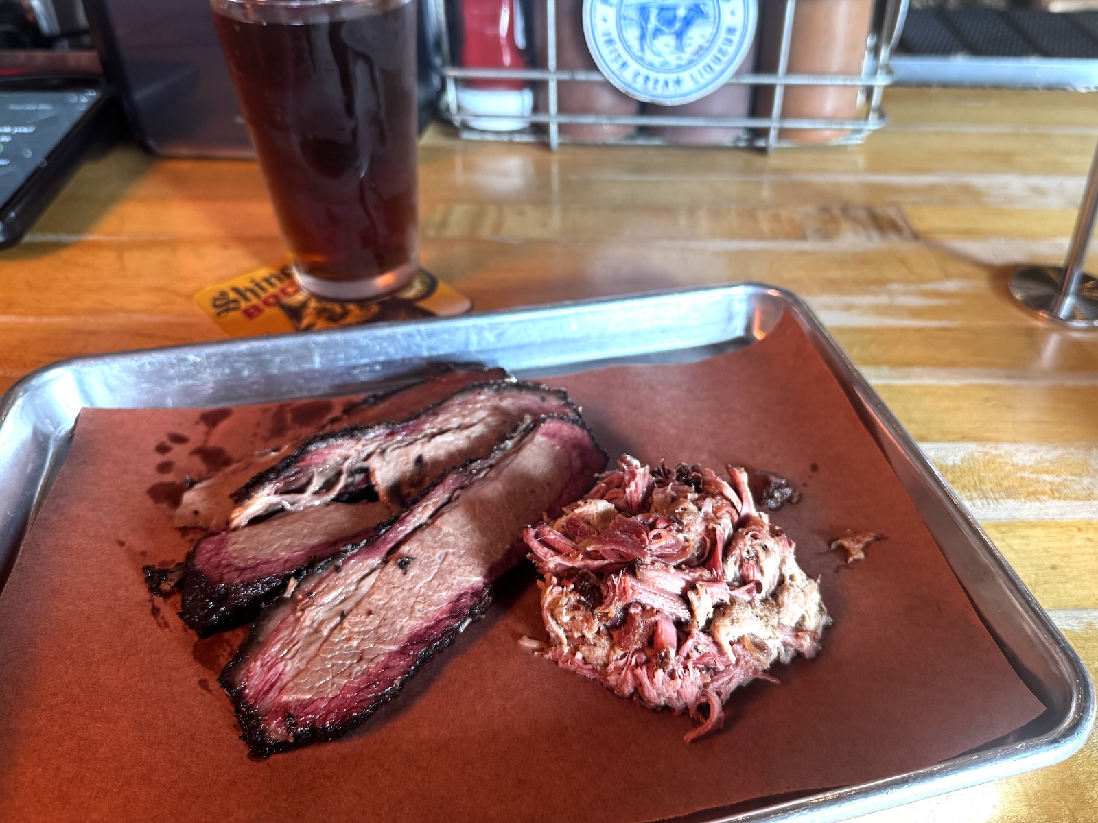 Sliced smoked brisket and a pile of pulled pork on a metal tray with a paper liner.