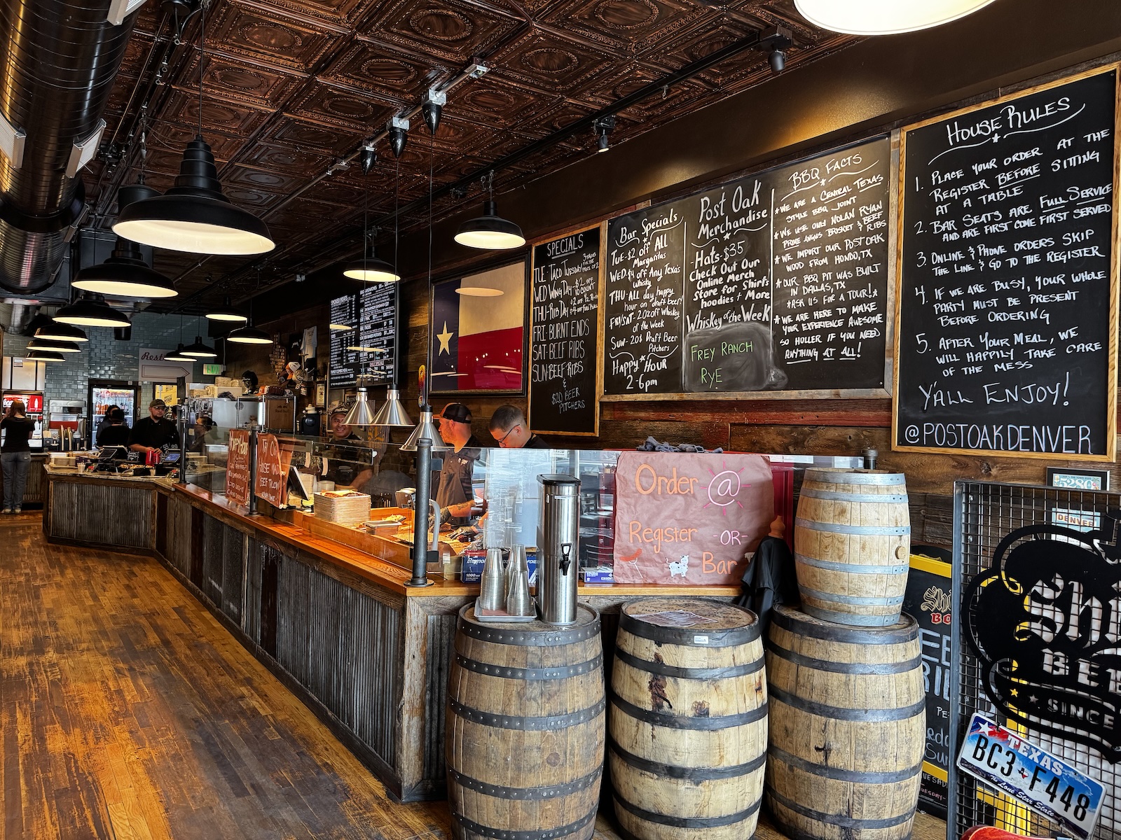 Inside a barbecue restaurant with a serving counter, wood floors, stacks of whiskey barrels, and chalkboard menus.