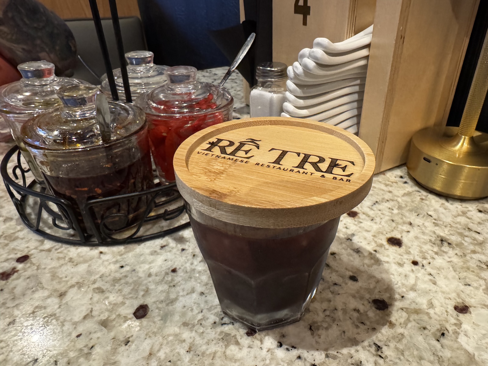 A cocktail in a rocks glass with a wooden lid stamped with the words Rễ Tre